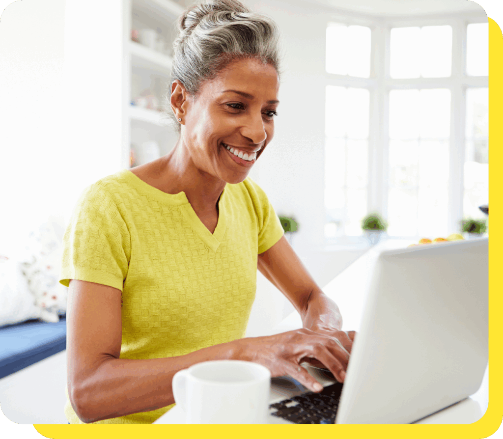 A woman smiling warmly while seated at a desk, using her laptop to explore a credit union loan calculator.