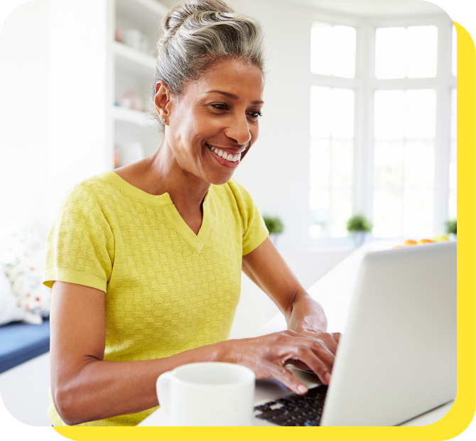 A woman smiling warmly while seated at a desk, using her laptop to explore a credit union loan calculator.