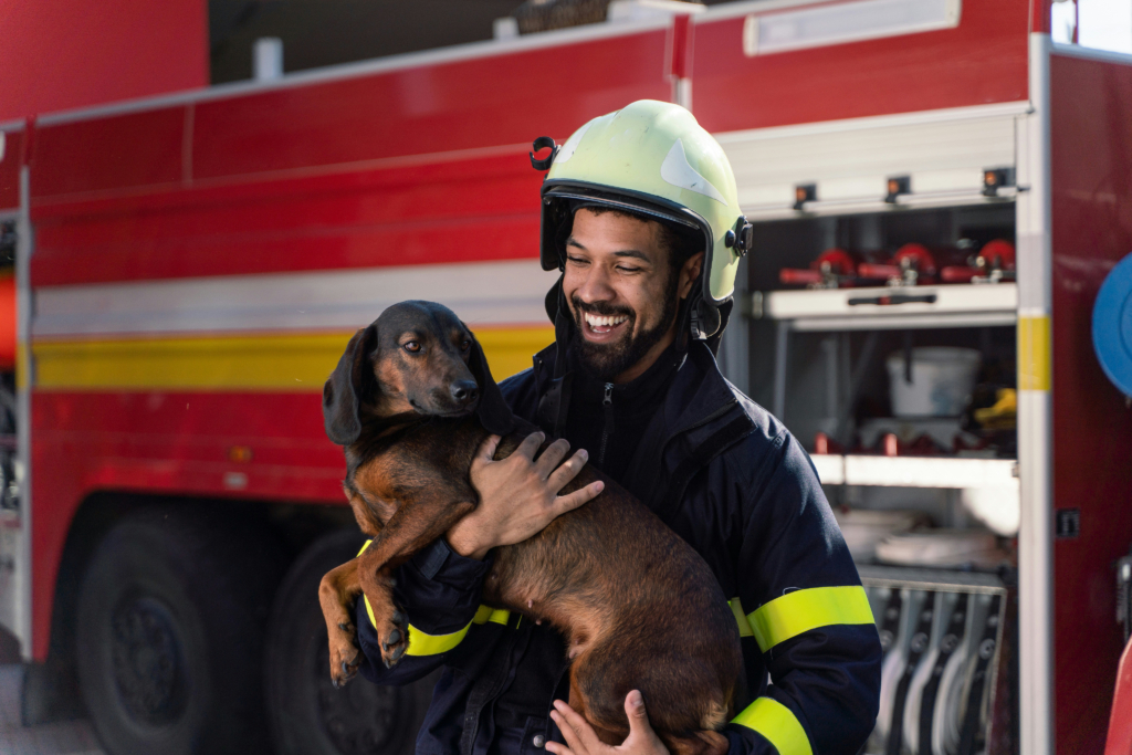 Smiling firefighter in uniform holding a rescue dog, showcasing community service and care.