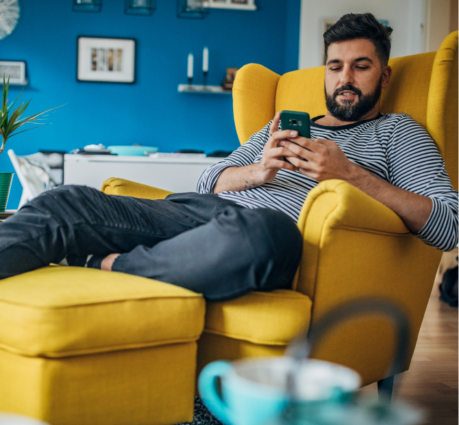 Man relaxing on a chair while using his phone, enjoying the stability of a fixed rate savings account.
