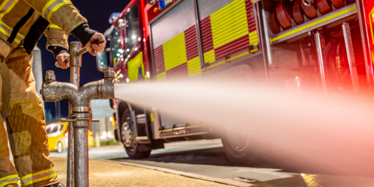 Firefighter spraying water with fire truck in the background