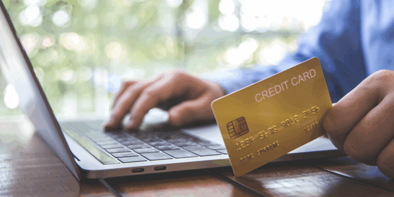 Close up of a hand holding a credit card while the other hand types on a laptop