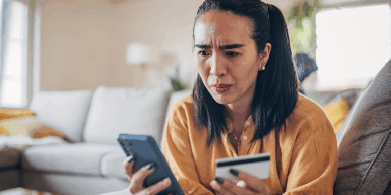 Dark-haired woman lying on sofa using mobile phone and holding credit card