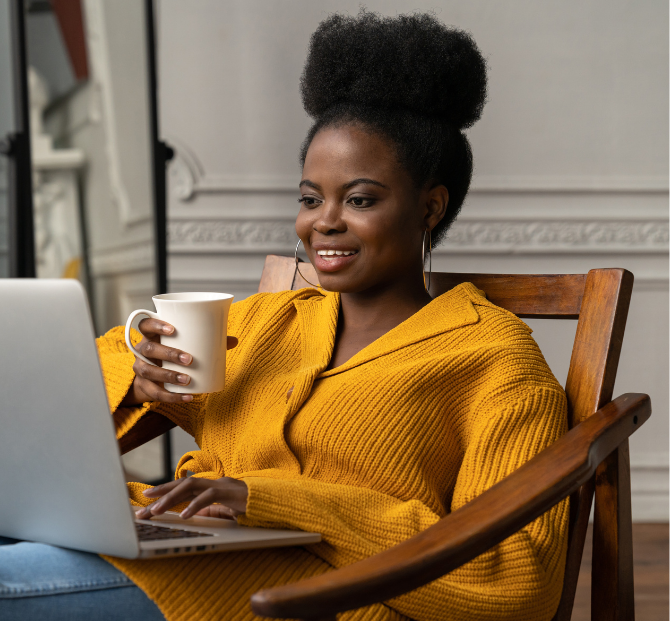 Woman smiling warmly whilst holding a coffee mug and reading about Serve and Protect Credit Union on her laptop, discovering how payroll deduction can help manage her finances effortlessly.